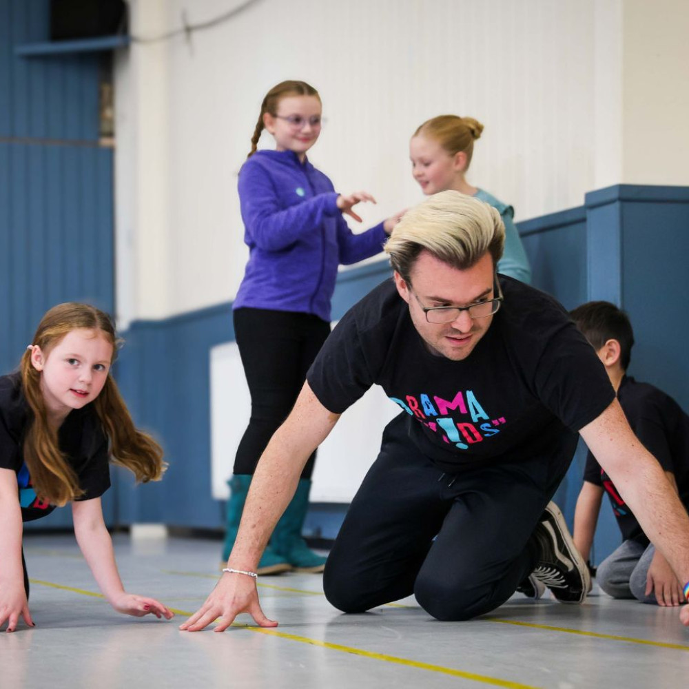 A Drama Kids teacher and children taking part in an imaginative movement exercise on the floor